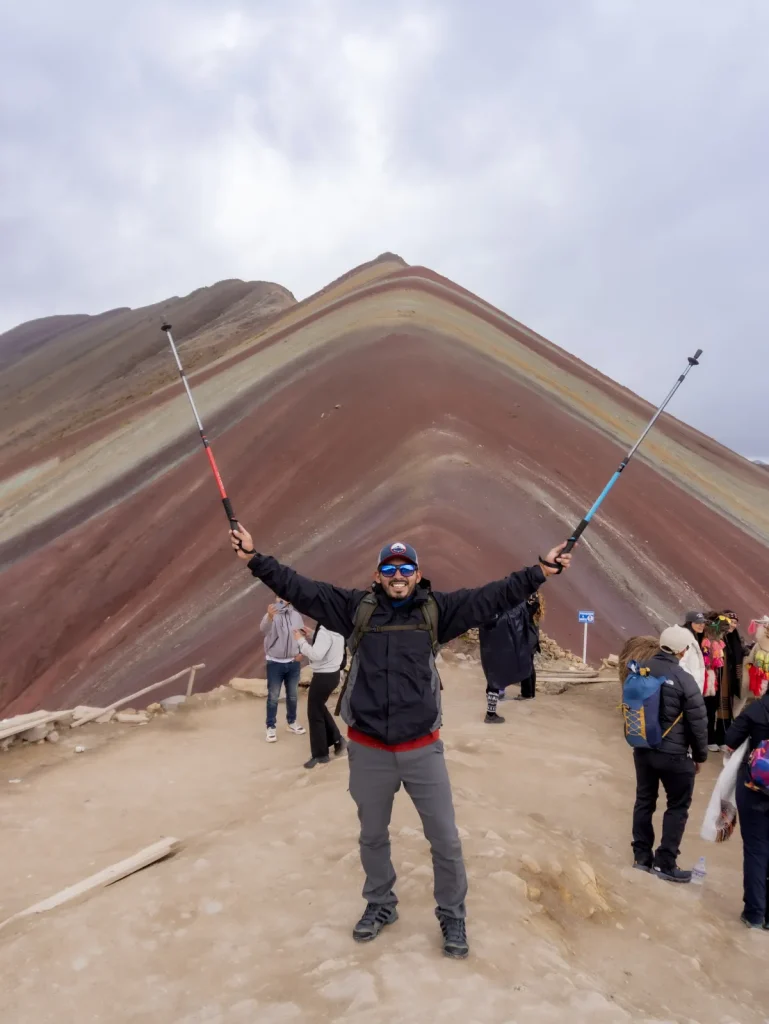Excursionista celebrando con bastones en la cima de Vinicunca, la Montaña Arcoíris de Cusco